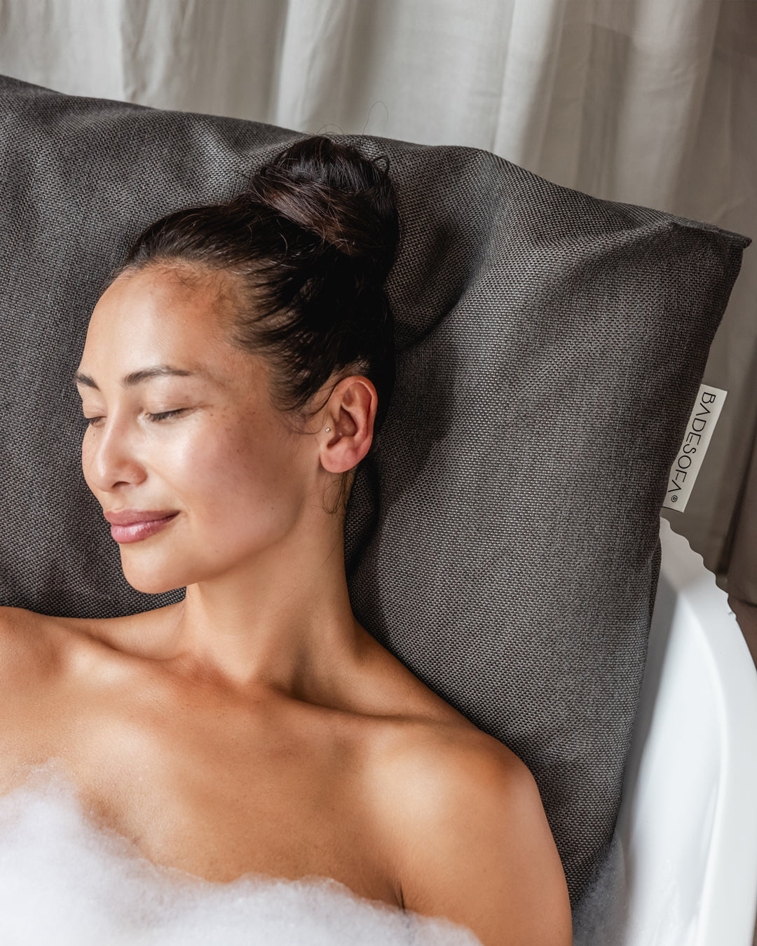 Mocha Badesofa Rückenkissen (Size Large) in einer freistehenden Badewanne, mit lächelnder Person, die sich entspannt anlehnt. $ Freistehende Badewanne | Size Large