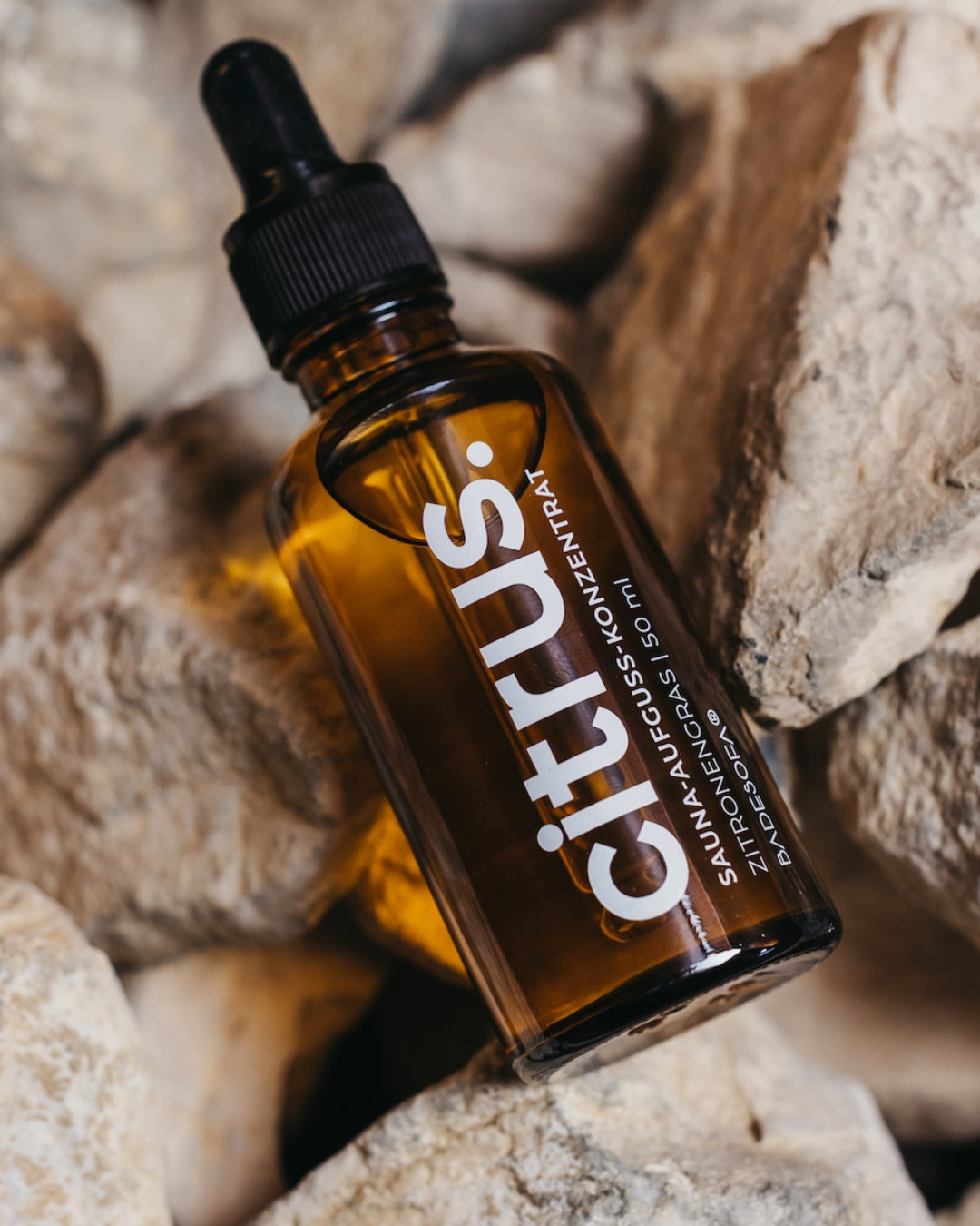 Fläschchen mit dem Saunaaufguss-Konzentrat Citrus liegt auf Saunasteinen.