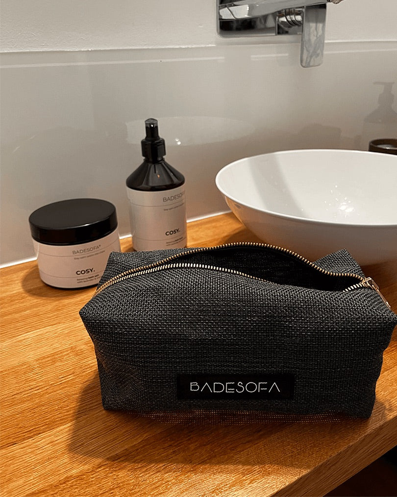 Geöffnete Kosmetiktasche in Anthrazit steht neben einem Waschbecken.