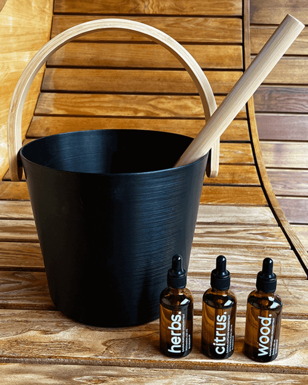 Saunakübel, Kelle und drei Fläschen mit Saunaaufguss-Konzentrat stehen auf einer Saunabank.